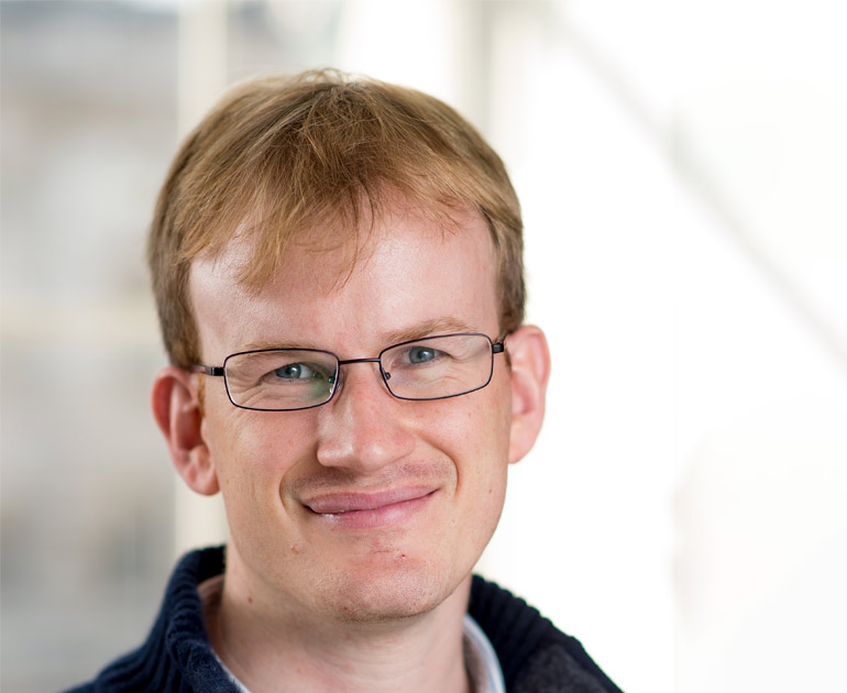 The head and shoulders of James Grande looking at the camera against a white background. He has short, ginger hair and glasses. He is smiling.