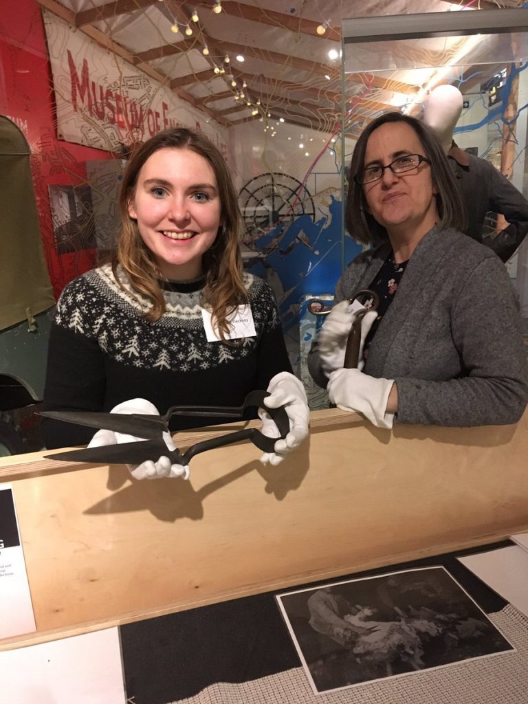 Two volunteers at the object handling trolley in the MERL gallery holding up metal tools