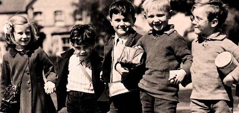Five children/evacuees standing in a row, smiling in the sun