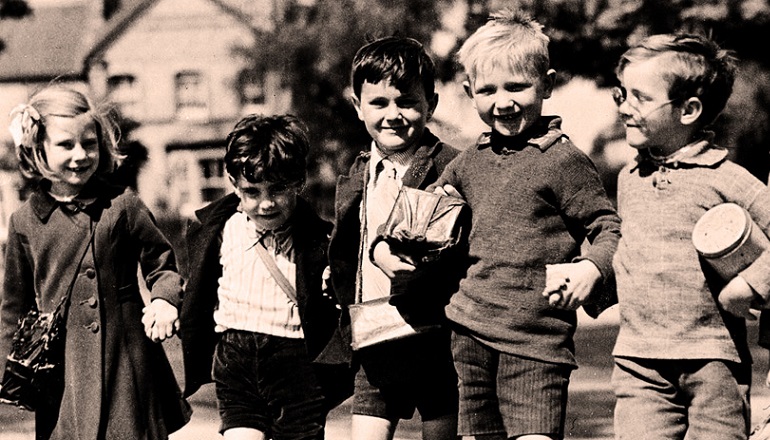 Five children/evacuees standing in a row, smiling in the sun