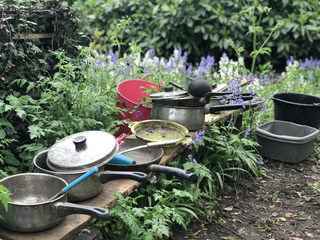 muddy pots and pans on a bench in the wooded area surrounded by bluebells