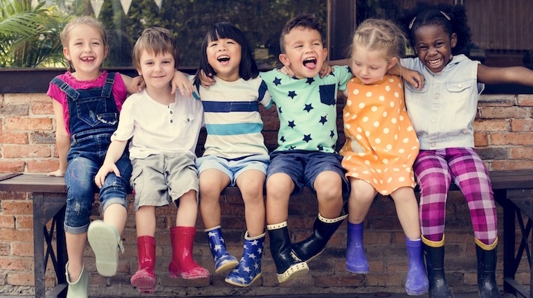 Smiling children in colourful summer clothes and wellies sitting on a bench