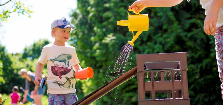 Children play with a watering can in the MERL garden in summer