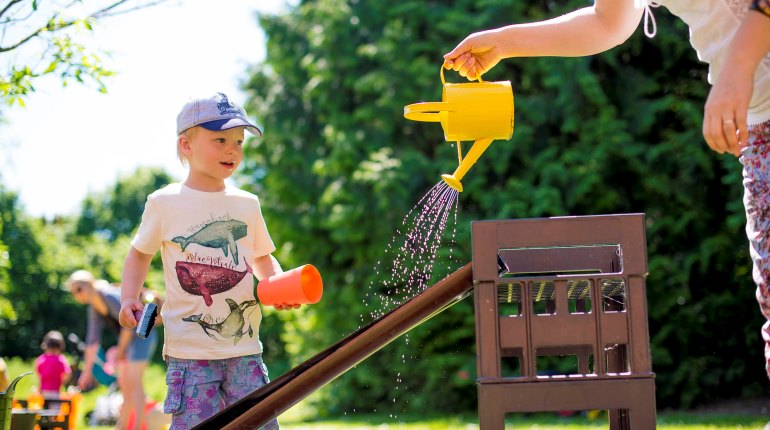 Children play with a watering can in the MERL garden in summer