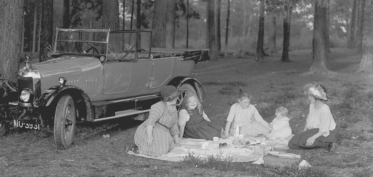 Black and white photograph of a family having a picnic next to a car in the woods