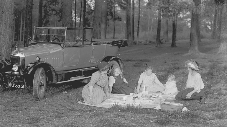 Black and white photograph of a family having a picnic next to a car in the woods