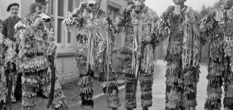 Black and white photograph of men dressed as mummers drinking pints