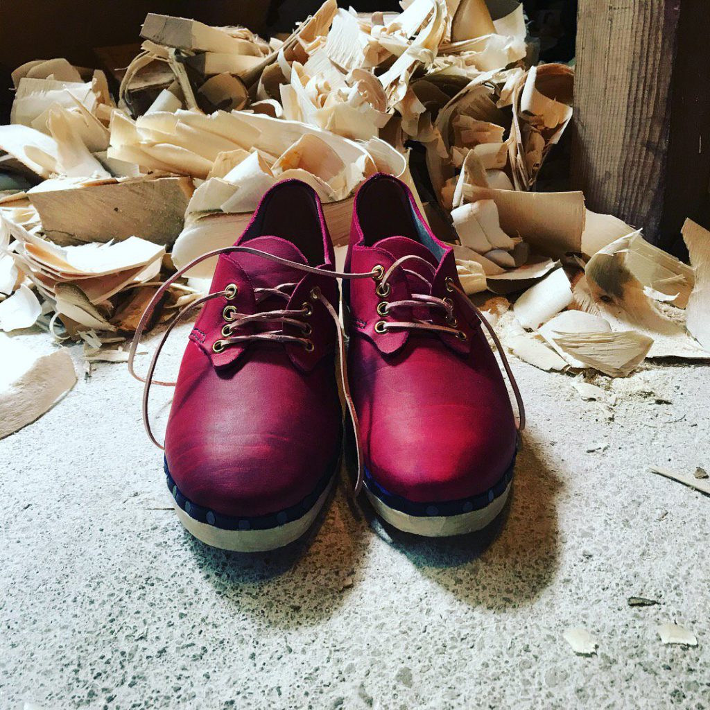 The brand new pair of dark pink leather lace-up clogs made for Hannah James with wooden soles with piles of wood shavings