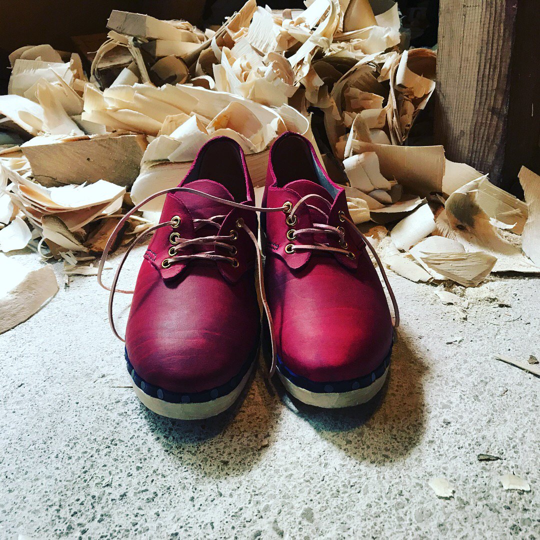 The brand new pair of dark pink leather lace-up clogs made for Hannah James with wooden soles with piles of wood shavings