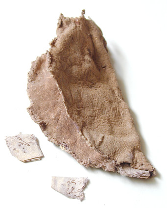 A beige, circular leather poch, with hand-stitching around its edge. The pouch is folded in half, and is in a poor condition, with split edges. The pouch contains scraps of paper with illegible ink writing. The ink is slightly brown in colour. 