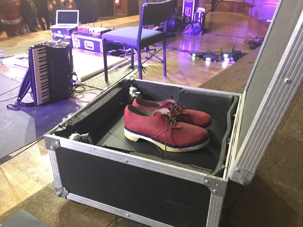 Hannah James' new red dancing clogs in a metal kit box on stage after the MERL Annual Lecture, with accordion in the background