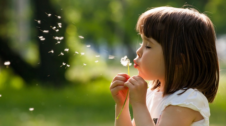Profile of a girl blowing seeds off of a dandelion