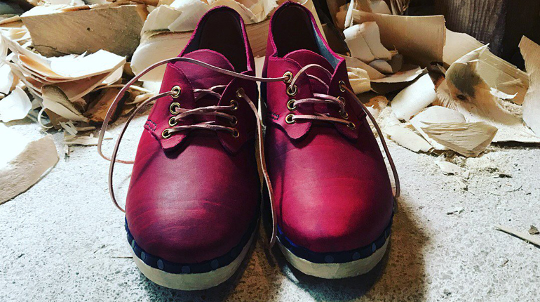 New pair of dark pink leather lace-up clogs with wood shavings in the background