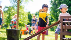 Two toddlers playing with a watering can at a picnic in the MERL garden