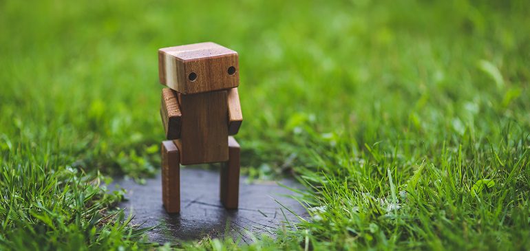 Small wooden robot figure standing in grass