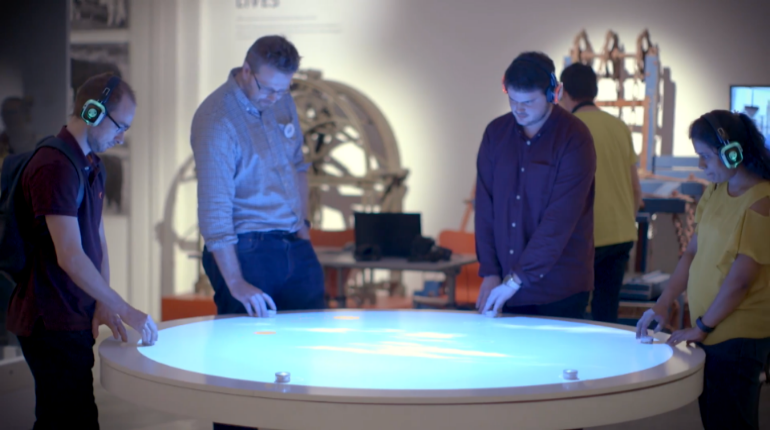 Four people standing around the interactive table in the OCL gallery