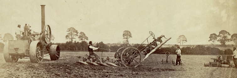 Black and white photograph showing a Fowler steam engine powering a cable plough in a field.