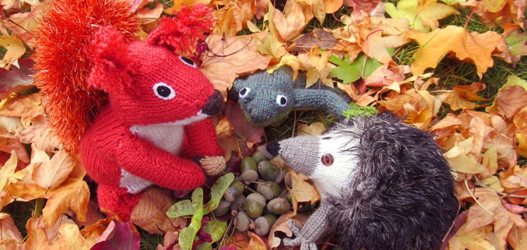 Knitted hedgehog poking its face out from a bed of colourful leaves for Autumnal Animals event