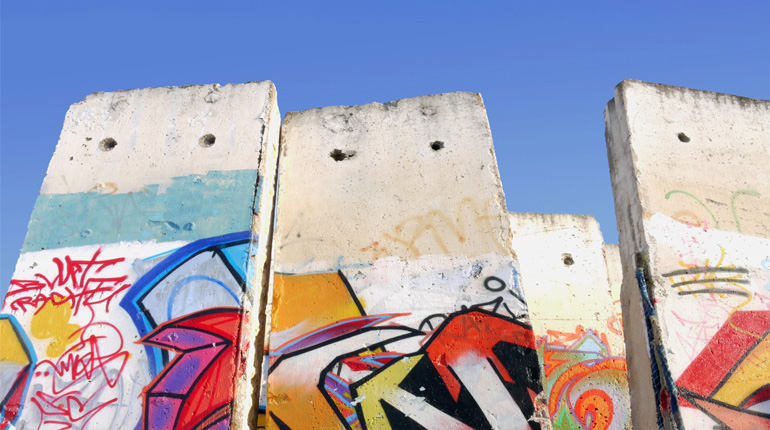 A section of the Berlin Wall with brightly coloured graffiti against a blue sky for the Popular Protest event