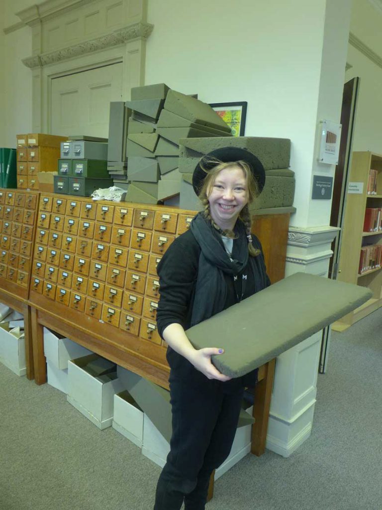 Student in standing in front of archive drawers holding a book mount