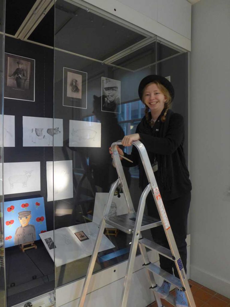 Student standing on a step ladder in front of a glass case with artwork