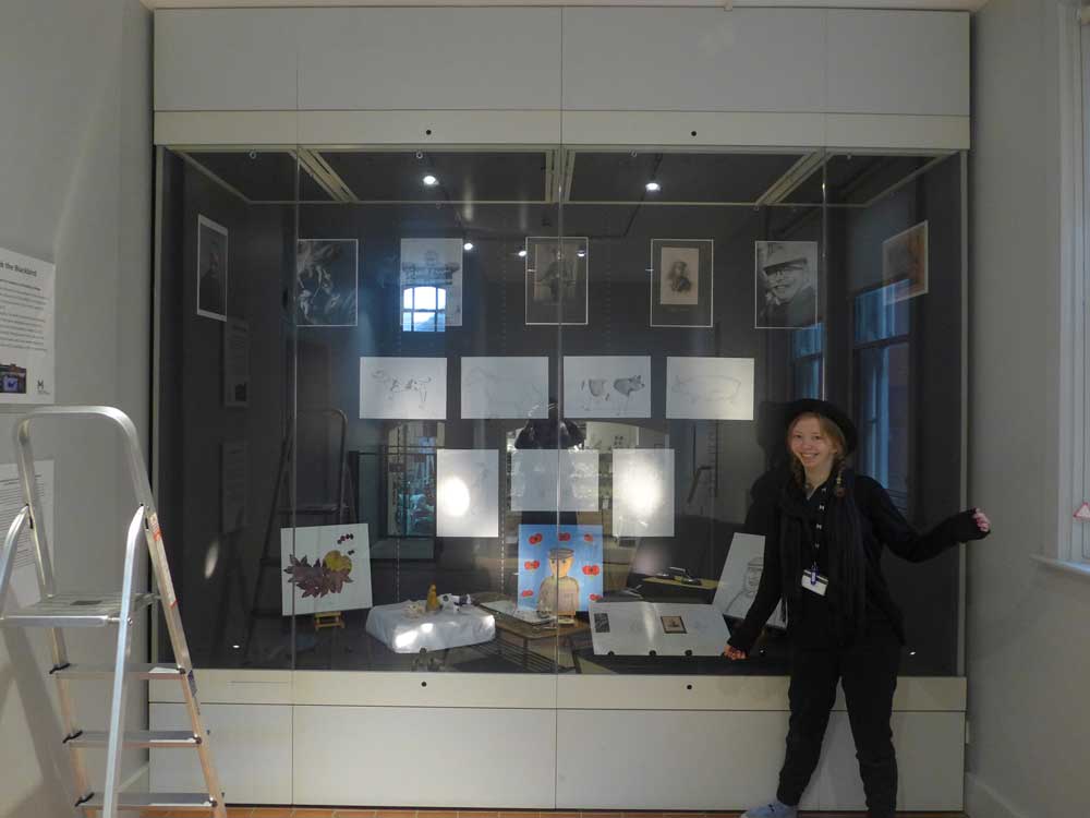 Student standing in front of a glass case displaying archive images and her own artwork