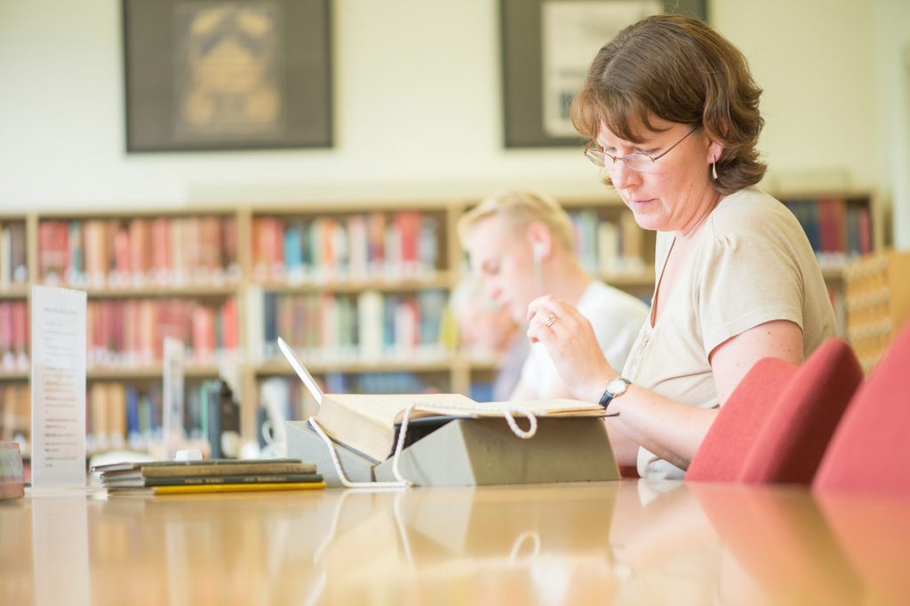 A women with brown curly hair looks at a book in the Museum reading room.