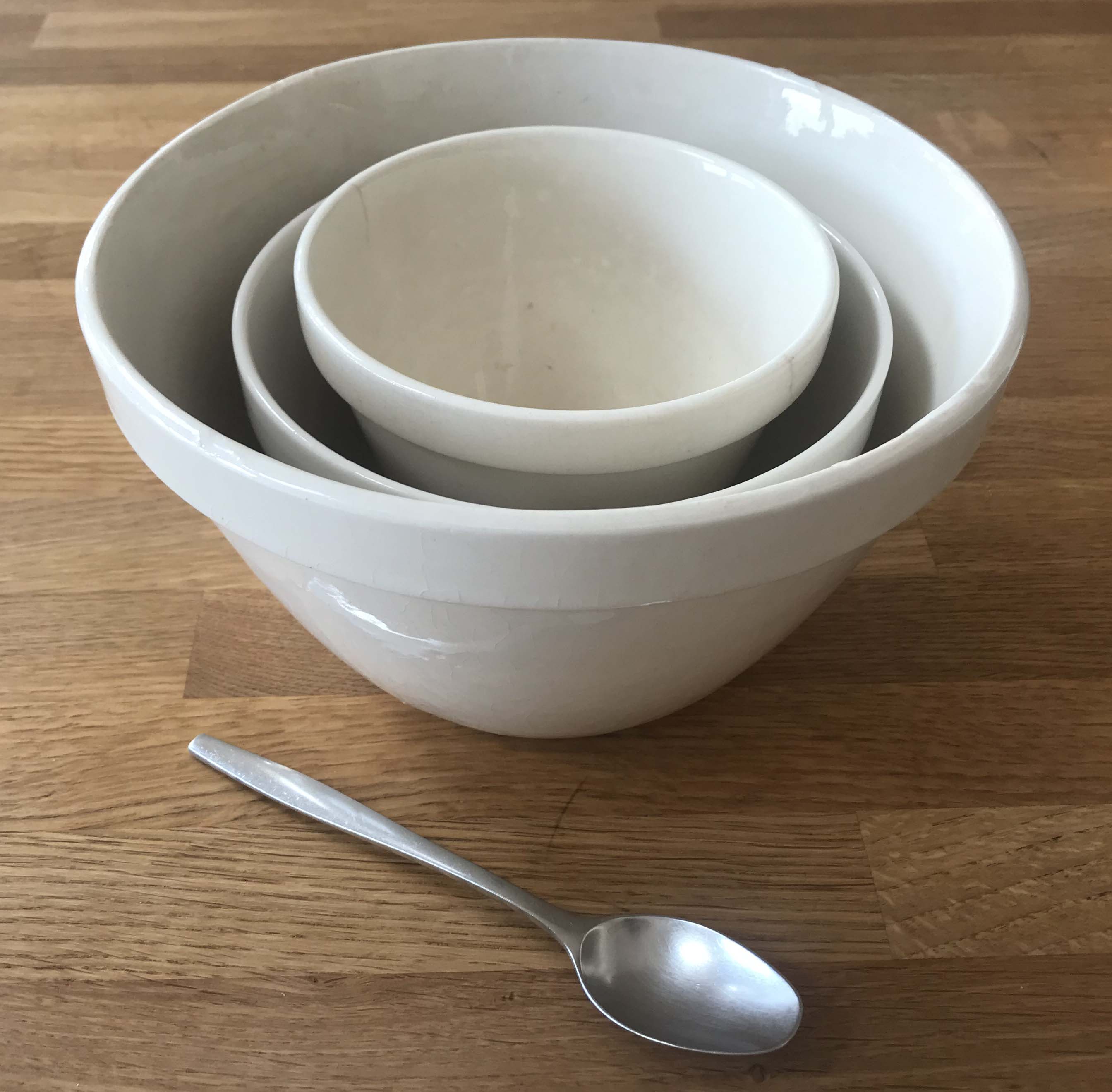 A stack of three white pudding bowls and a spoon on a kitchen worksurface