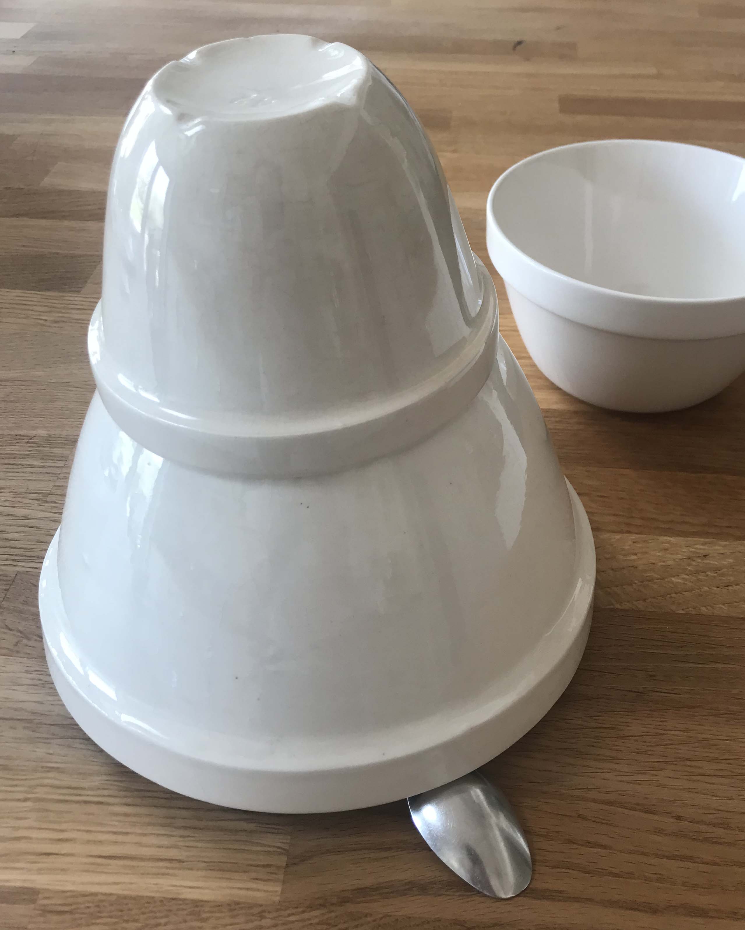 Small upturned bowl on top of larger upturned bowl with one edge raised and sitting on a spoon on a kitchen worksurface