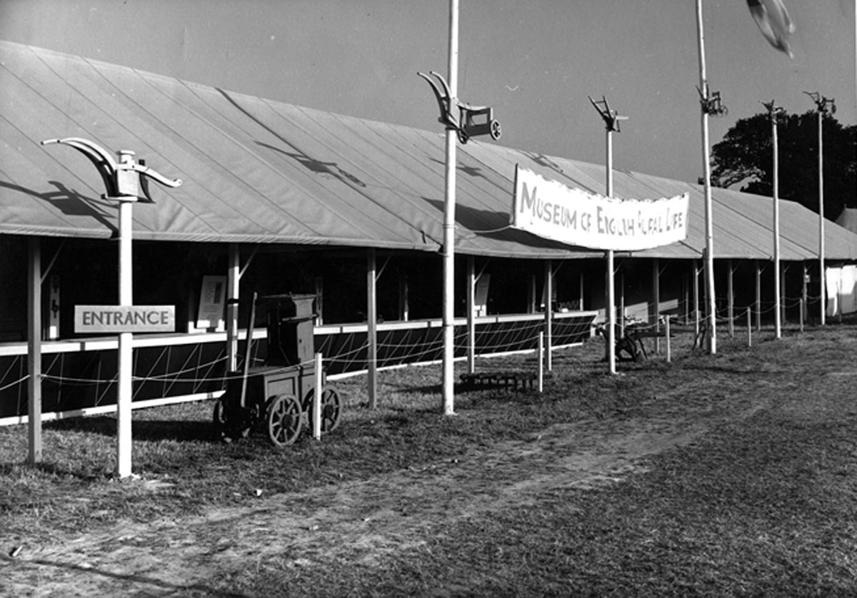 A long trade stand stretches into the distance with model ploughs mounted on flagpoles in front of the stand and a fence