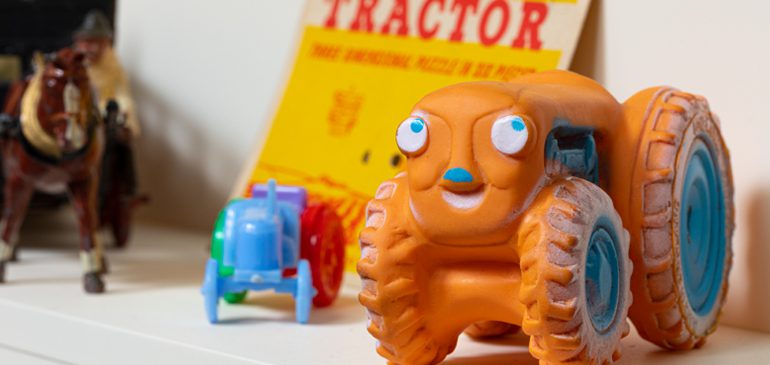 a bright orange toy tractor with facial features from the farm toys collection at the MERL