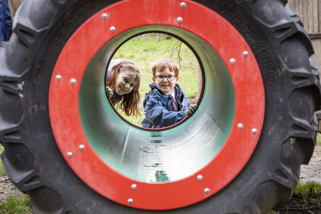 Two children looking through a tractor wheel