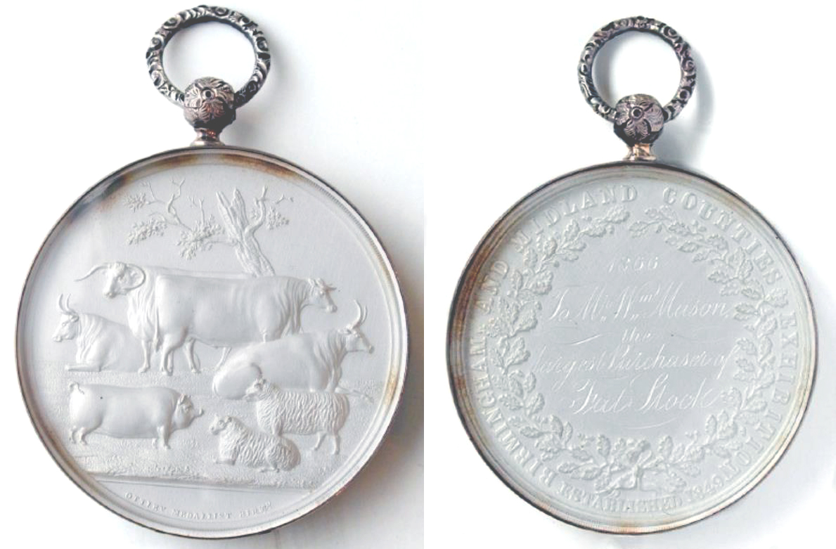 Two faces of a white medal encased in a silver ring. Features a relief picture of farm animals on one face and engraved text on the other face.