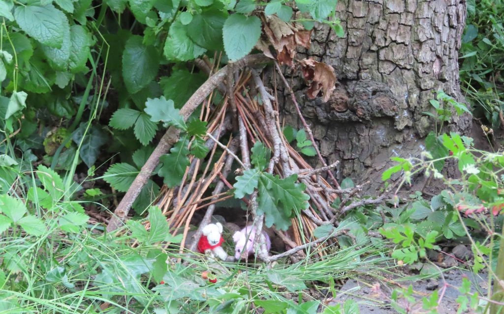 Twig den up against a tree with crocheted sheep inside 