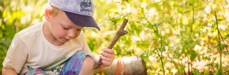 a boy crouches in the woods playing with a stick