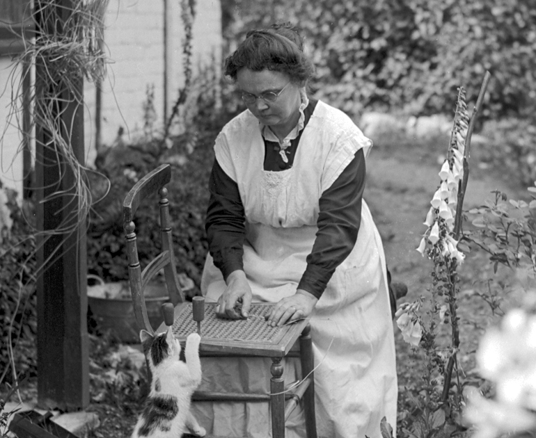 Woman caning a chair in garden with cat.