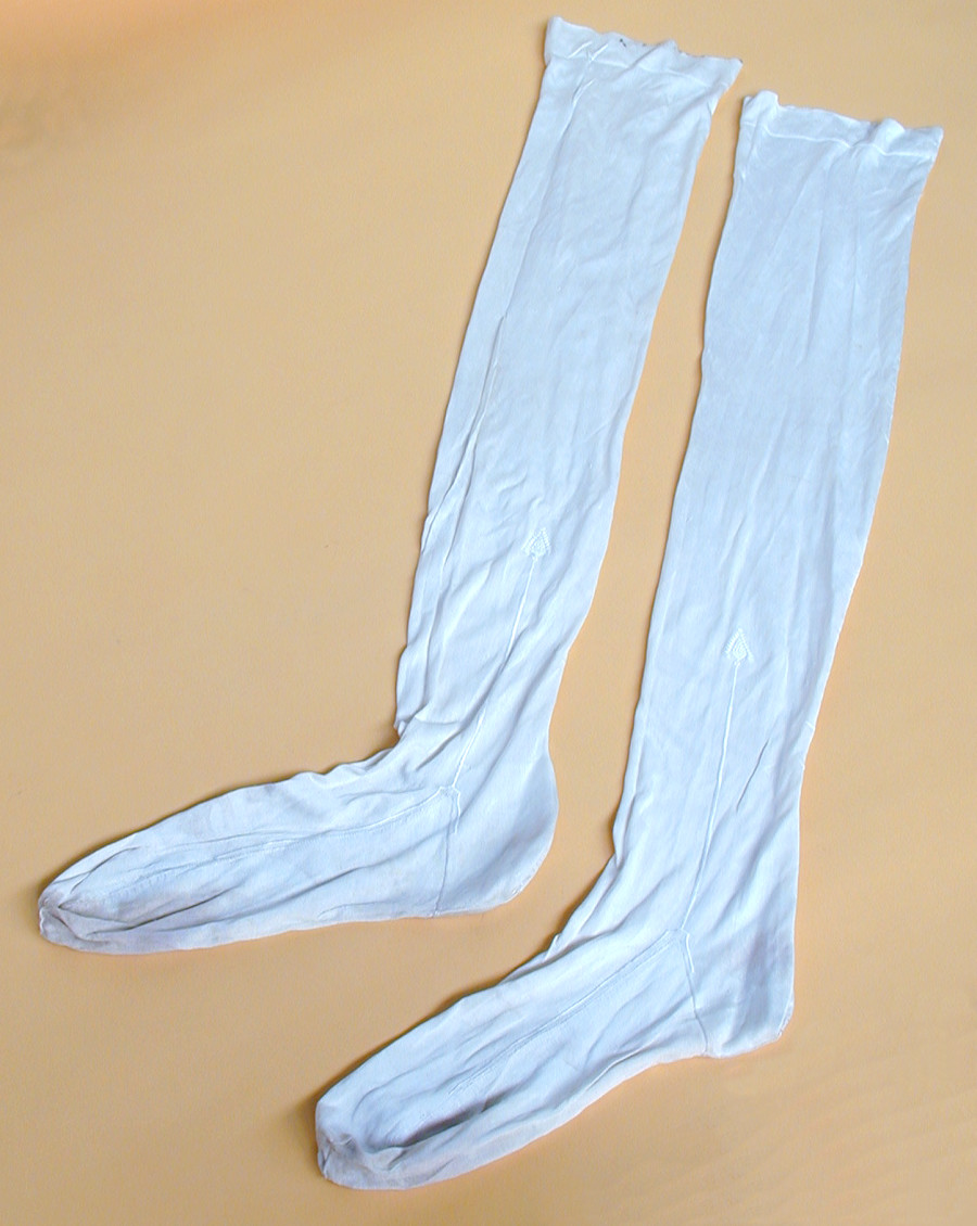 These stockings are part of a coachman's livery. This livery was used by Mr Harvey Thomas's father, Henry, and was worn between 1896 and 1904 when Henry was coachman to the High Sherif of Berkshire, Mr Arthur Harvey Thursby. The uniform consisting of jacket, waistcoat, trousers, stockings, top hand and accessories. These stockings are made of knitted silk hase with small embroidered design on each side. They also have cream colour. (MERL 92/74/7)