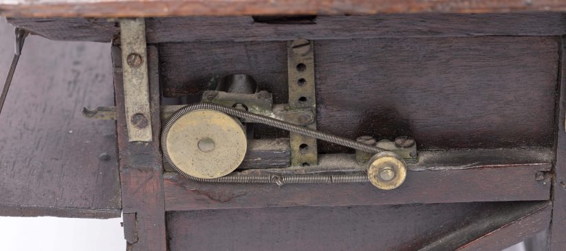 Detail of a small dark wooden threshing machine mechanism with cogs and workings visible.