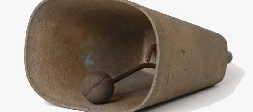 Metal sheep bell with handle, seen on its side with clapper visible