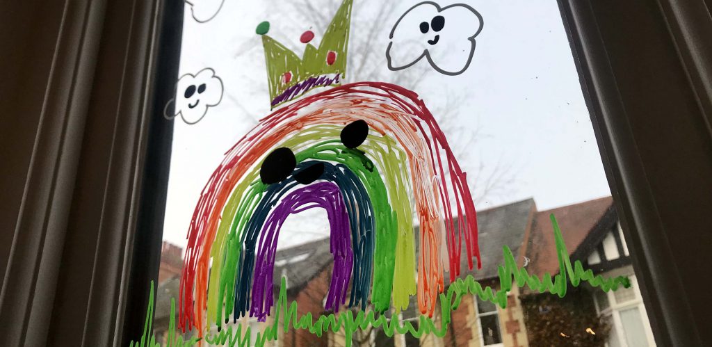 A colourful smiling rainbow drawing on a winodw, with red brick houses in the background