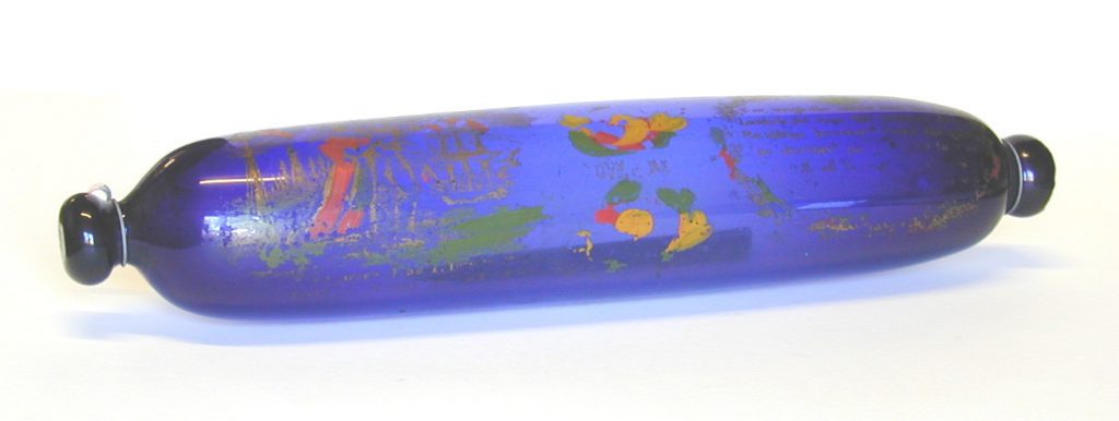 A rolling pin, made from blue glass. It is decorated with green, gold and red paintwork.