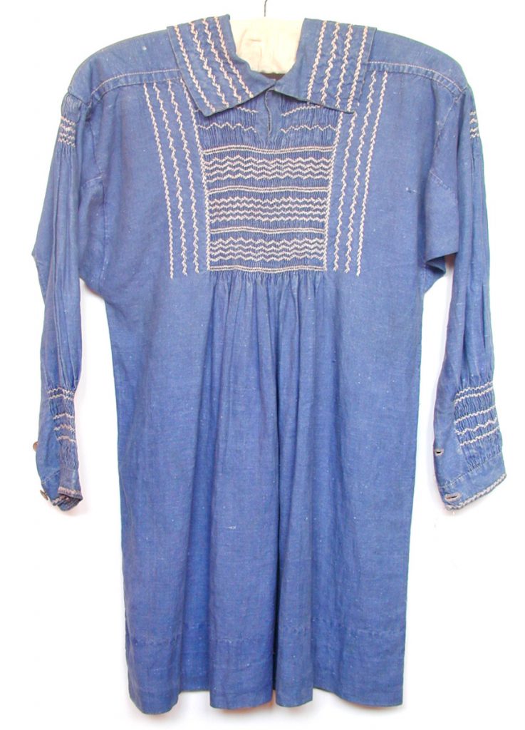 A blue, long sleeved smock dress, with stitching that appears white and brown in colour