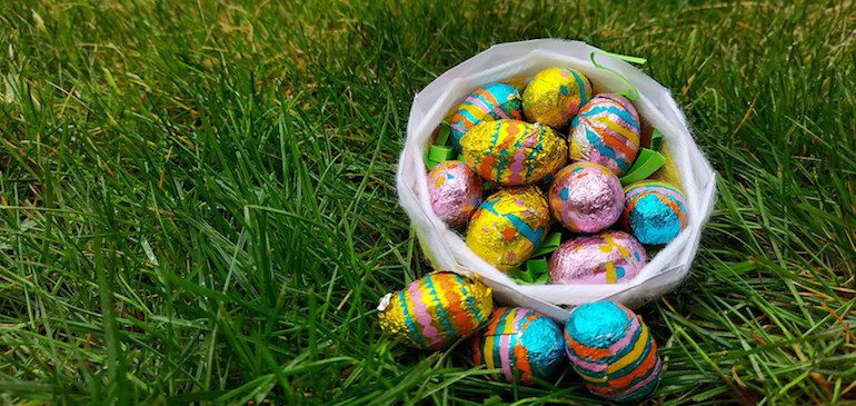 Basket sitting on grass filled with colourfully wrapped Easter eggs