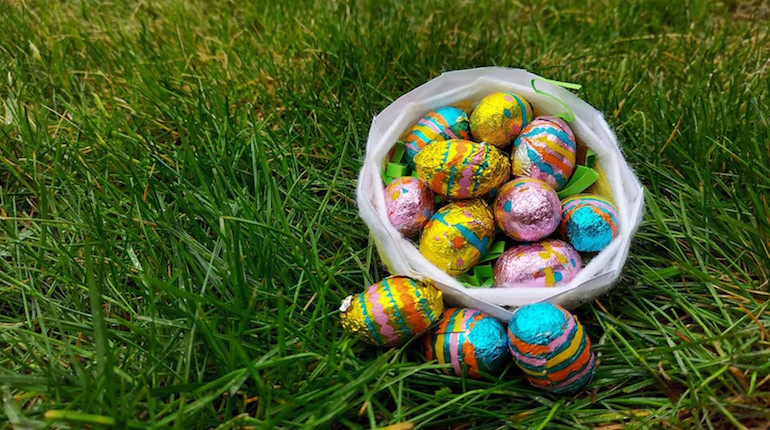 Basket sitting on grass filled with colourfully wrapped Easter eggs