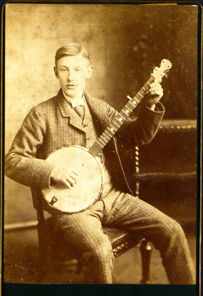 A sepia image of a young man sitting on a chair holding a banjo