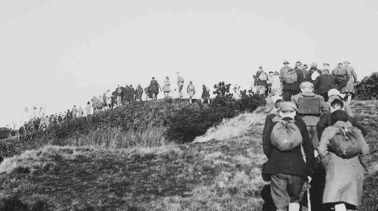 Black and white lantern slide of people walking on a hill