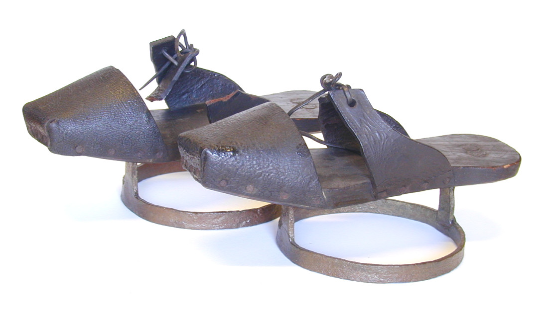 Pattens are wooden shoes with an iron hoop beneath that were used by most countrywomen as overshoes to keep their feet out of the mud in the farmyard and around the dairy. These pattens have a wooden sole with leather toe caps and side pieces, and are riveted on to an iron ring. The laces are missing.