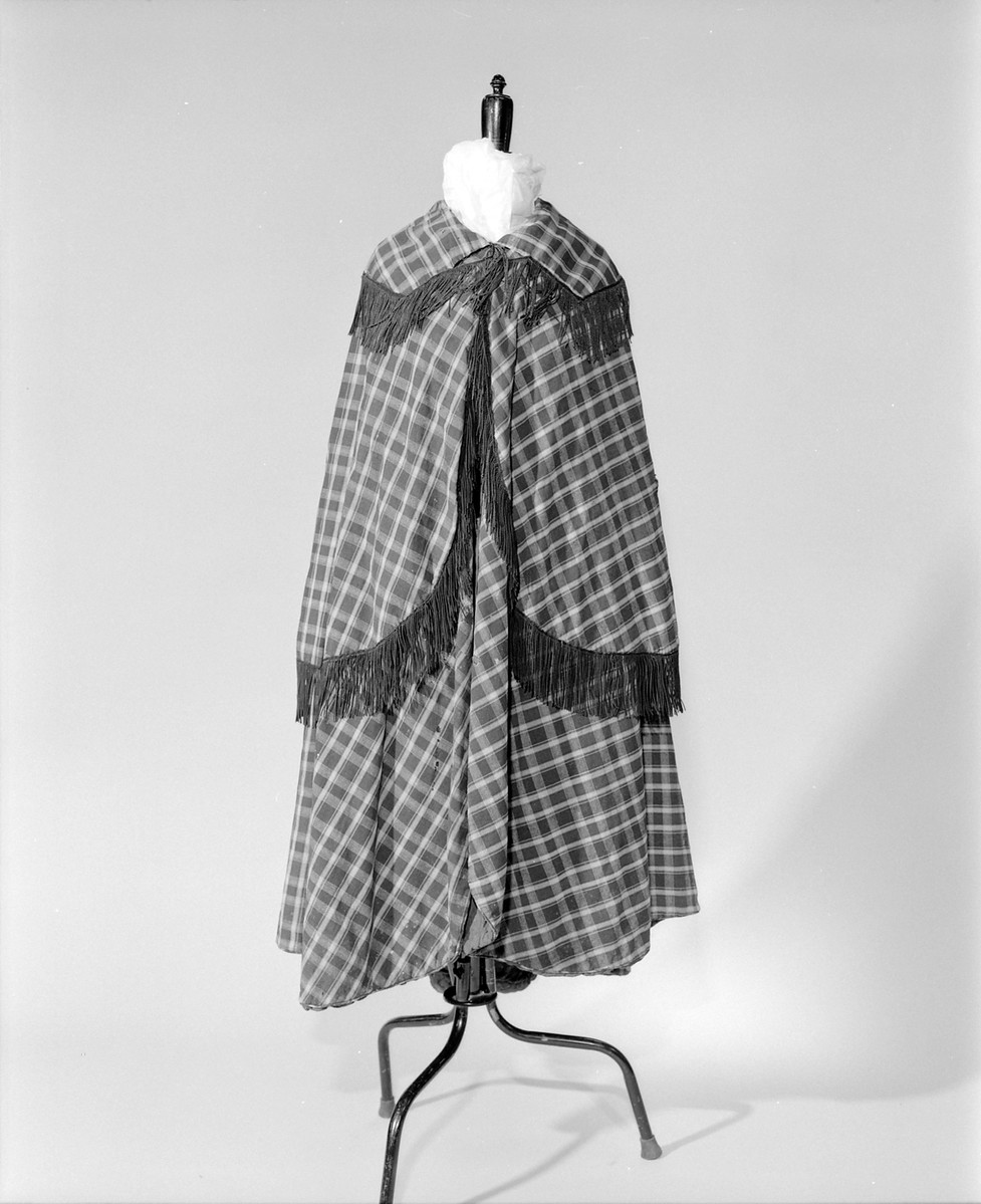 This cloak, referred to by the donor as a Victorian Ulster, belonged to the Pavier Family of Basingstoke, Hampshire. It is a very full cape, of brown and blue plaid, with a plain blue lining and brown fringing along the collar and sleeves. (60/52)