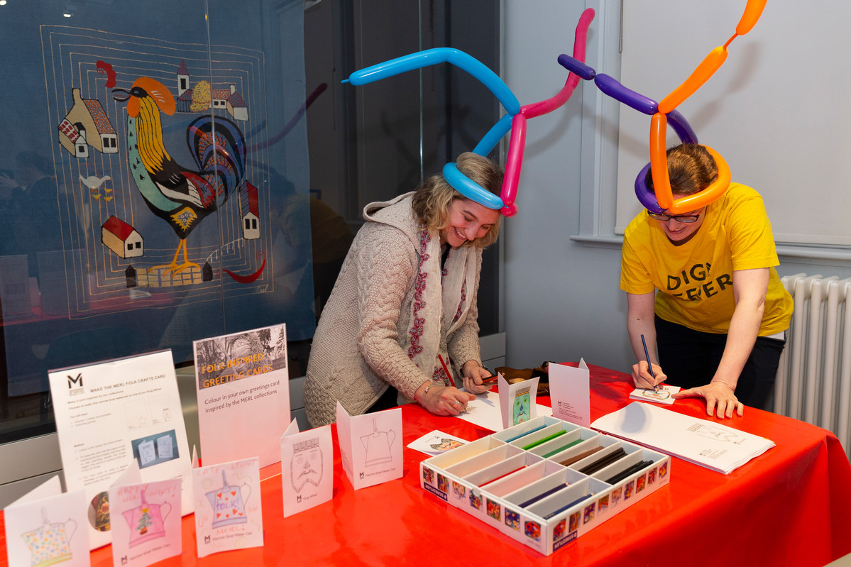 Two people wearing balloon hats and writing greeting cards.