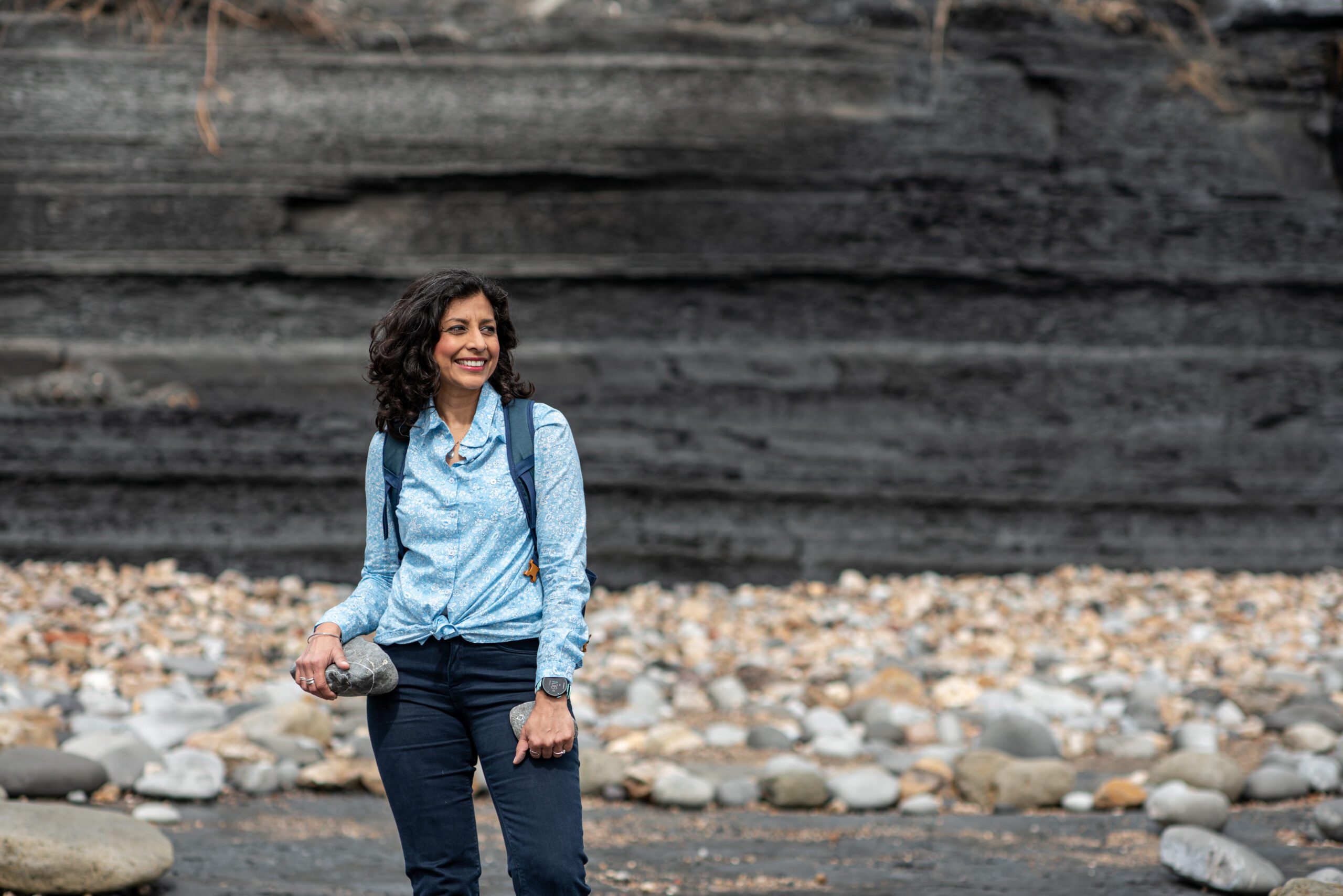 Dr Anjana Khatwa holding a stone by a cliff.
